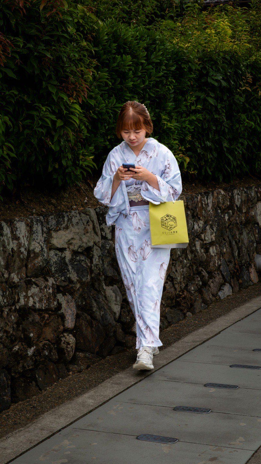 ai彼女 日本語-桜並木でスマートフォンを見つめる女性、AI彼女と日本語で会話する日常のイメージ